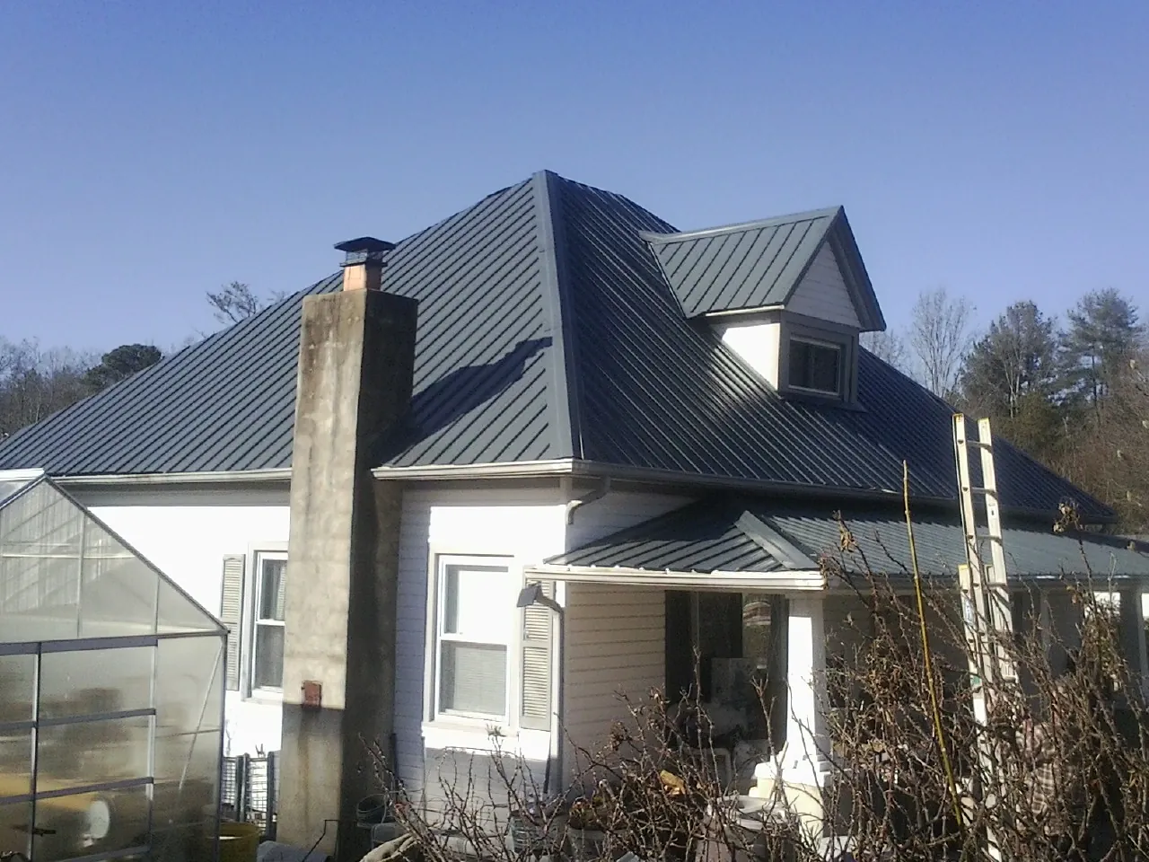 Dark blue standing seam metal roof on a white farmhouse with dormer — Slate & Tile Roof Repair by Roofing Brothers in Alcove
