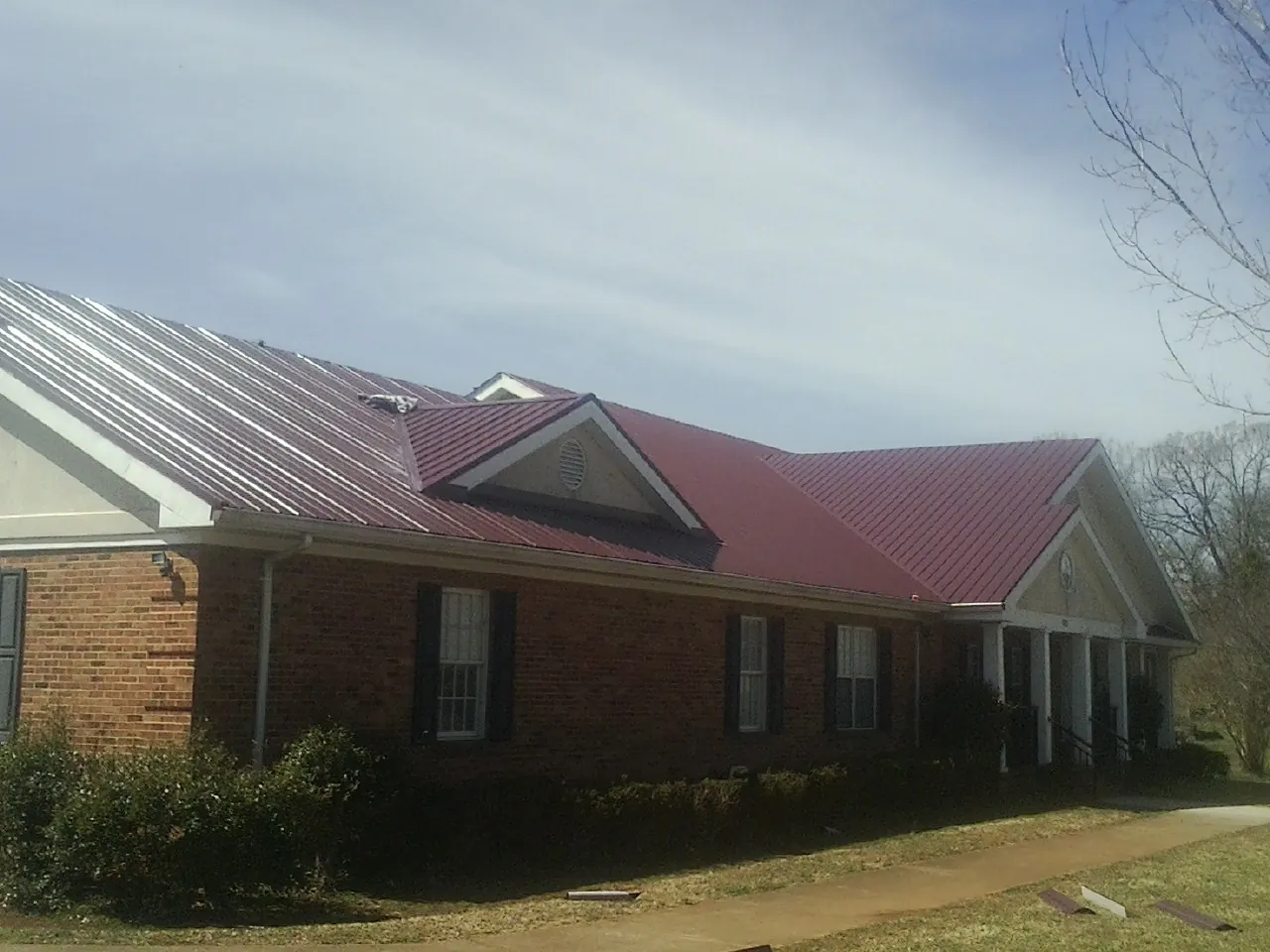 Red metal roof with gabled entries on a long brick building, from a Hail Damage Roof Repair job in Alcove