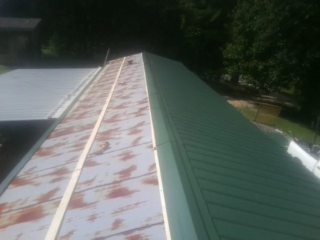 Old rusted panels beside newly installed green metal roofing — Wind Damage Roof Repair by Roofing Brothers in Alcove