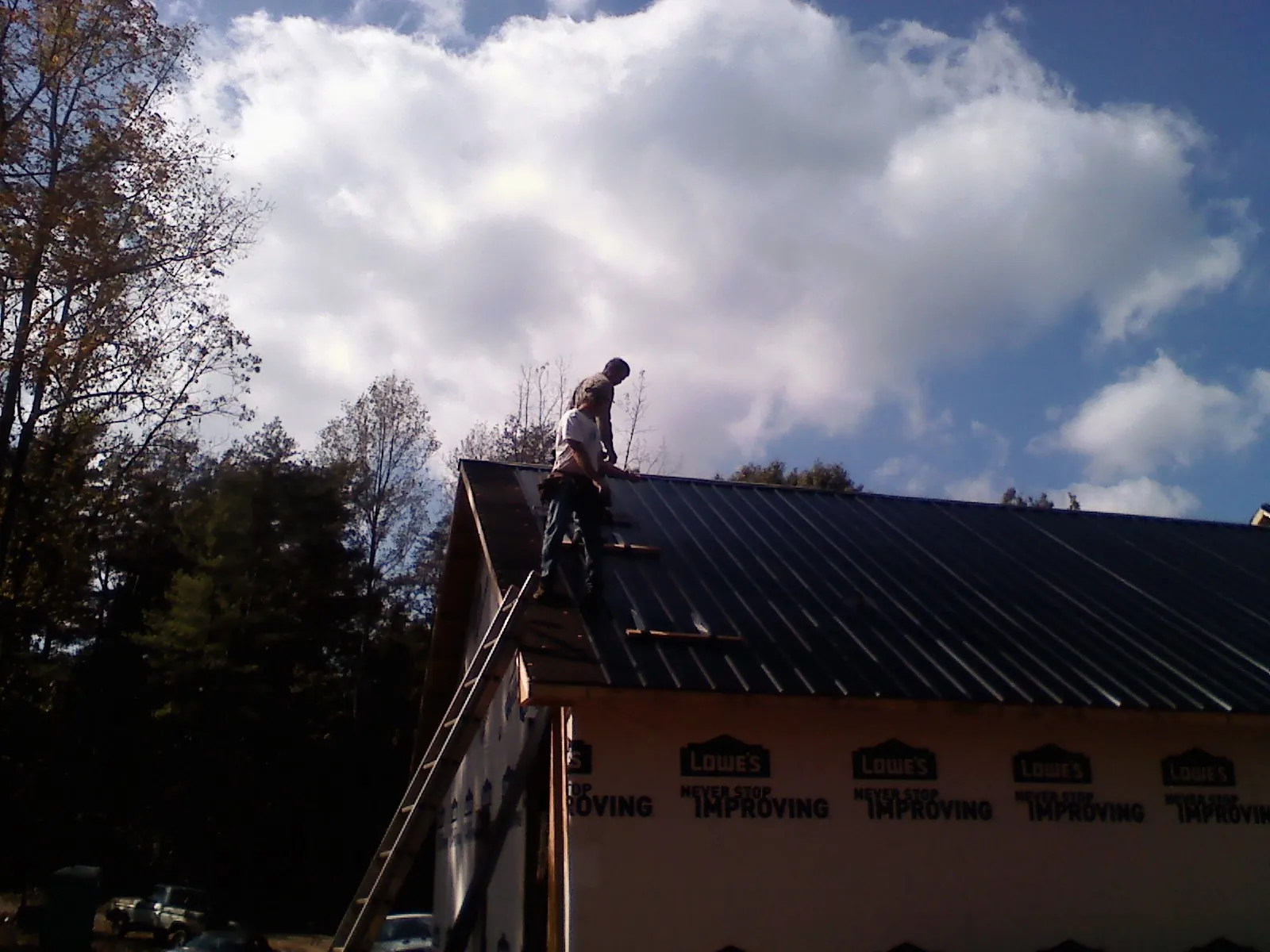 Roofer fastening dark metal panels high against a cloudy sky, from a Roof Inspection job in Alcove