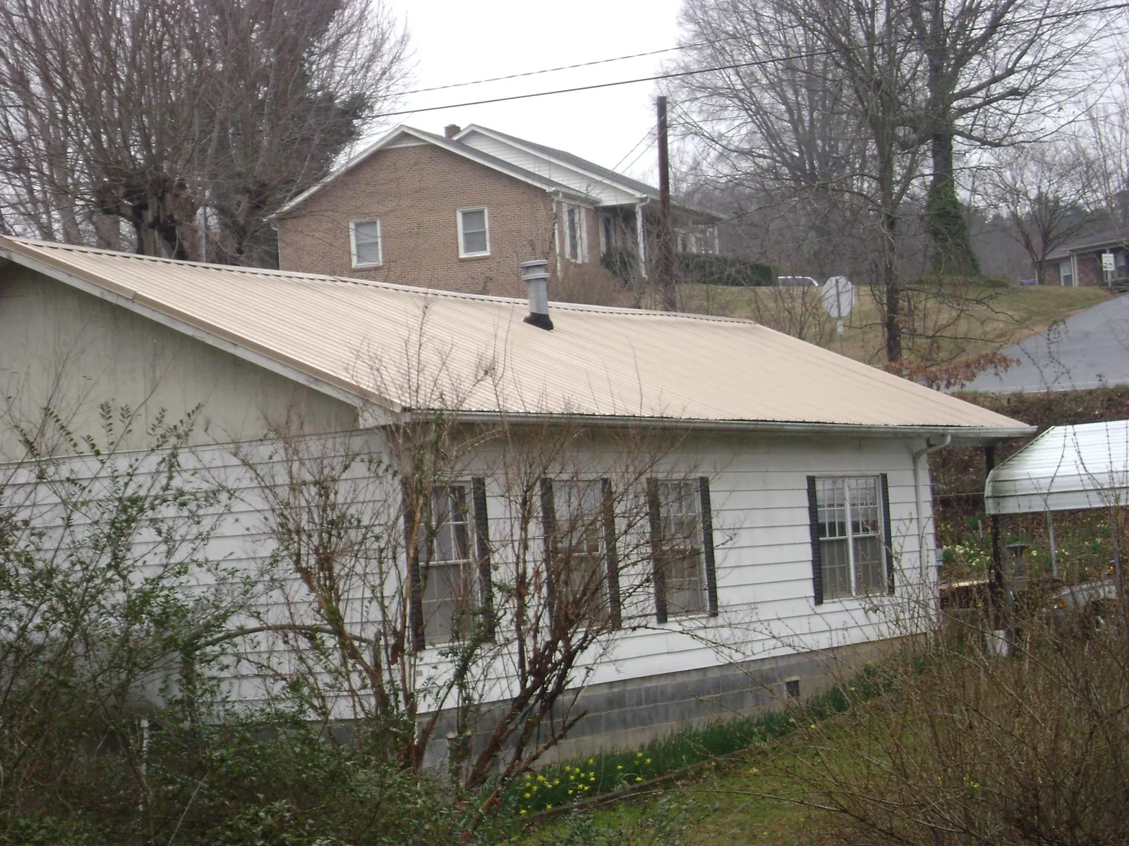 Tan metal roof on a white sided house set into a hillside — Commercial Roofing by Roofing Brothers in Alcove