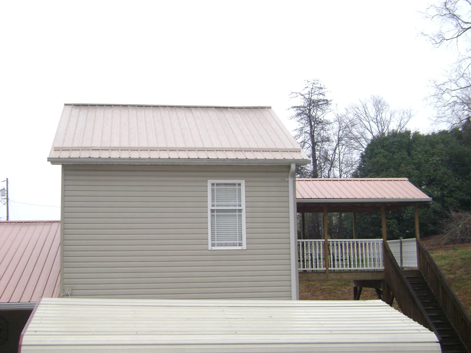 Tan metal roofs on a two story addition and attached porch, from a Roof Replacement job in Alcove